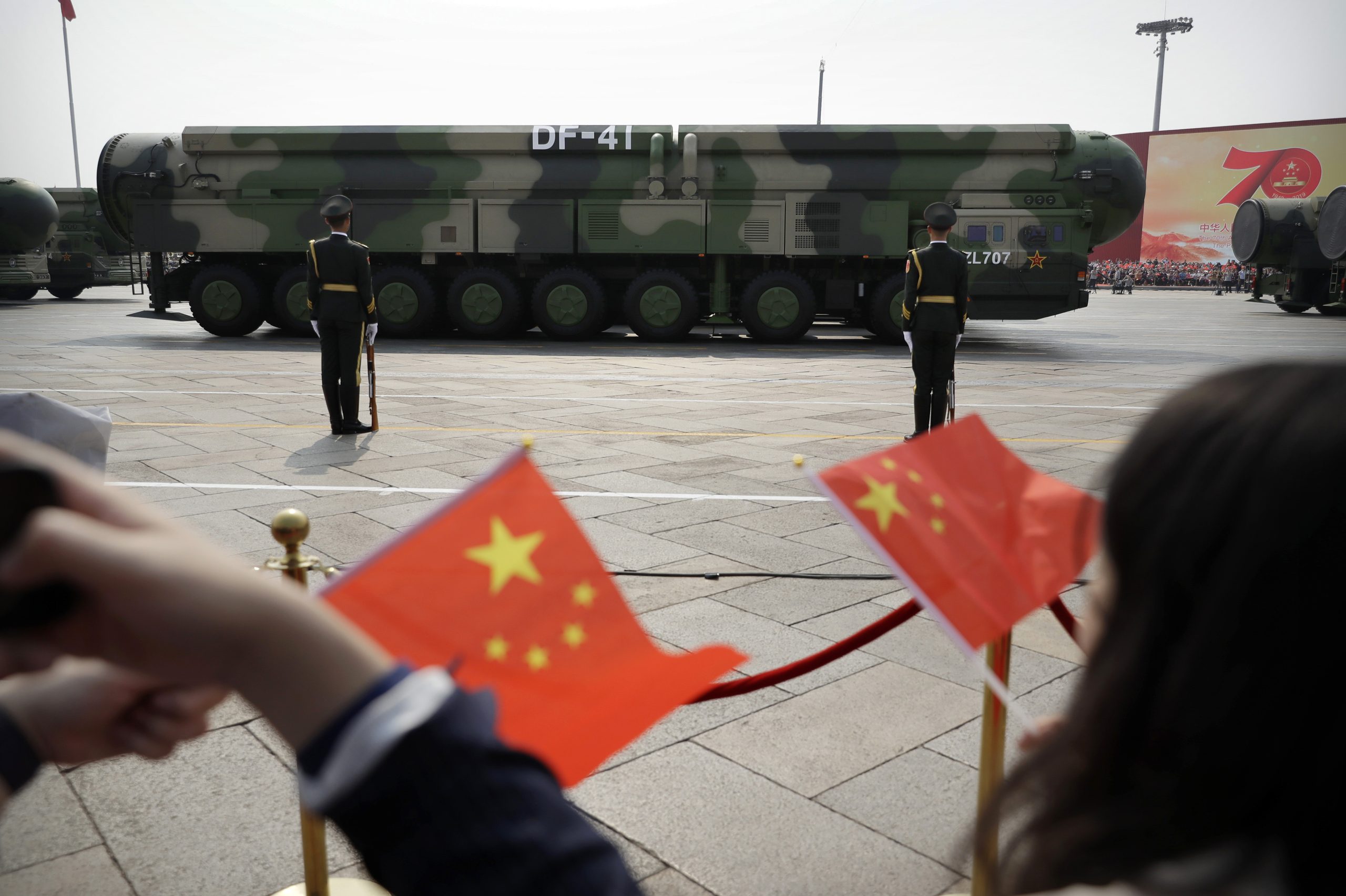 Espectadores acenam com bandeiras chinesas enquanto veículos militares carregando mísseis balísticos DF-41 desfilam durante uma parada para comemorar o 70º aniversário da fundação da China Comunista em Pequim - 1/10/19 | Foto: Mark Schiefelbein/AP