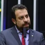 Guilherme Boulos durante discurso no plenário da Câmara dos Deputados; ele aparece com semblante que demonstra nervosismo; ele está de paletó cinza, gravata vermelha e camisa social azul claro