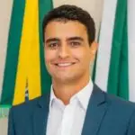 João Henrique Caldas, o JHC, aparece sorrindo em fotografia oficial como prefeito de Alagoas; atrás aparecem as bandeiras do Brasil, de Alagoas e de Maceió