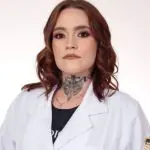 Carolina Arruda fazendo pose para a foto, com os cabelos ruivos e uma tatuagem no pescoço