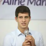 Imagem do prefeito João Campos com as duas mãos no microfone