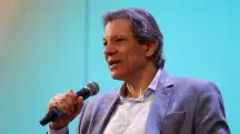 Fernando Haddad veste terno cinza com camisa branca enquanto discursa