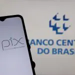 Celular com o app do Pix aberto, com a logo do Banco Central ao fundo