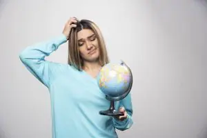 Menina loira com a mão na cabeça, pensativa, e segurando o globo terrestre na mão