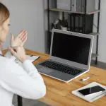 Mulher em frente a um notebook com o dedo apontando para a palma de sua mão, a fim de ilustrar linguagem de libras