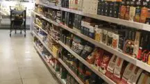 Imagem mostra gôndolas de um supermercado; ao fundo, um carrinho de mercado
