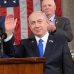 Benajmin Netanyahu com a bandeira dos EUA no fundo
