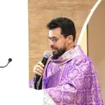 Padre de barba e batina roxa fala ao microfone