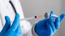 Imagem de pessoa, com luva azul, manipulando com seringa o frasco de vacina