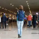 Imagem de saguão de aeroporto mostra pessoas nas filas. Em destaque uma garota com mochila nas costas.