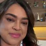 Imagem de Preta Gil com blusa florida rosa, preta e branca. Ao fundo objetos de decoração