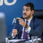 Jorge Messias segura o microfone sentado na mesa durante coletiva na AGU