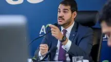 Jorge Messias segura o microfone sentado na mesa durante coletiva na AGU