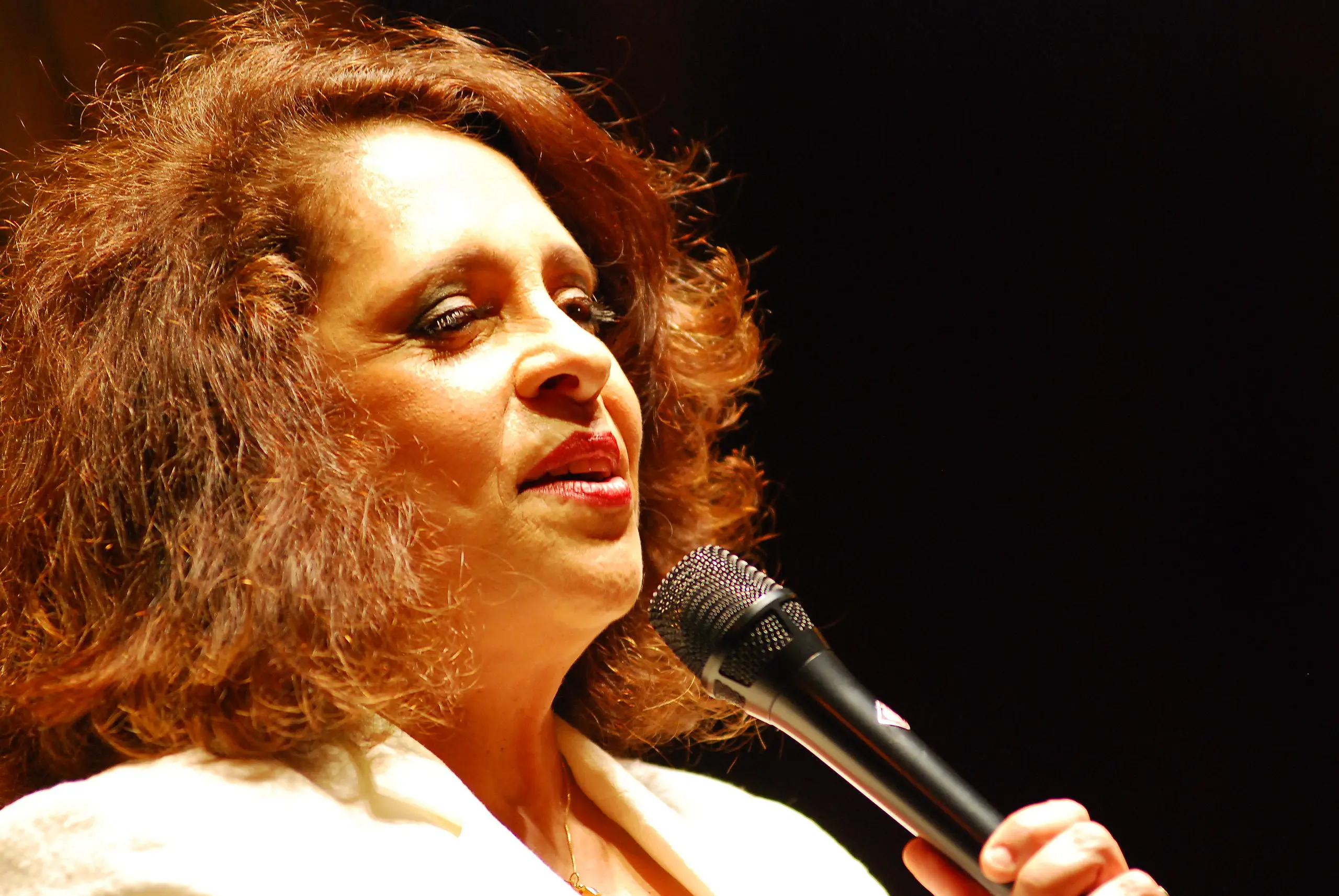 Gal Costa veste blusa branca e canta com microfone na mão