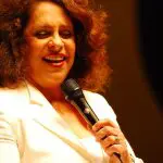 Gal Costa veste blusa branca e canta com microfone na mão