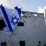 Homens israelenses penduram uma bandeira israelense sobre um prédio danificado, que foi atingido por um foguete do Líbano - 22/9/2024 | Shir Torem/Reuters