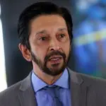 Prefeito Ricardo Nunes, de camisa azul e blazer cinza com fundo desfocado em azul