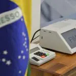 Urna eletrônica, usada nas eleições do Brasil, ao lado de uma bandeira do país