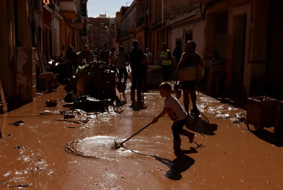 Criança remove lama da rua, depois de temporal na Espanha