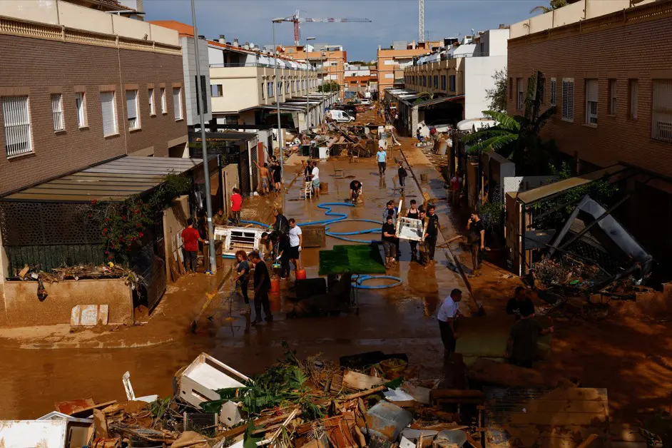 Pessoas limpam uma rua coberta de lama depois de temporal na Espanha