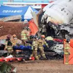 Bombeiros carregam o corpo de um passageiro dos destroços de uma aeronave que caiu depois de sair da pista do Aeroporto Internacional de Muan, em Muan, Coreia do Sul – 29/12/2024 | Foto: Kim Hong-ji/Reuters