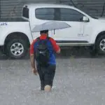 Homem caminha na chuva, em área alagada, em alusão ao alerta do Inmet