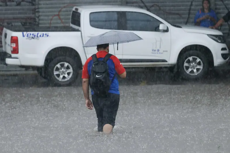 Homem caminha na chuva, em área alagada, em alusão ao alerta do Inmet