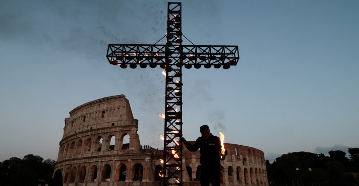 Um trabalhador acende uma cruz do lado de fora do Coliseu, antes da procissão da Via Crucis, durante as celebrações da Sexta-Feira Santa, em Roma - 18/4/2025 | Foto: Remo Casilli/Reuters