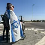 Um cidadão sentado com uma bandeira de Israel, em Kerem Shalom - 30/5/2025 | Foto: Shafiek Tassiem/Reuters