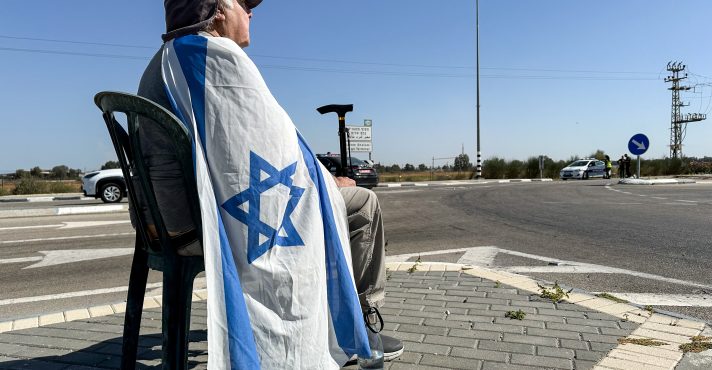 Um cidadão sentado com uma bandeira de Israel, em Kerem Shalom - 30/5/2025 | Foto: Shafiek Tassiem/Reuters