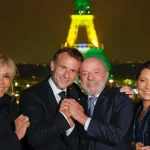 Lula e Janja posam ao lado de Emmanuel e Brigitte Macron, com a Torre Eiffel iluminada ao fundo nas cores da bandeira brasileira — símbolo do estreitamento de laços diplomáticos entre Brasil e França | Foto: Ricardo Stuckert/PR