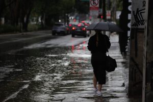 Pedestres enfrentam chuva forte, em alusão à nota sobre alerta vermelho do Inmet
