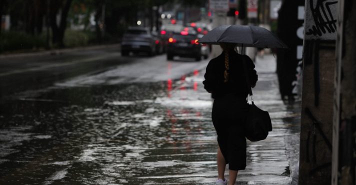Pedestres enfrentam chuva forte, em alusão à nota sobre alerta vermelho do Inmet