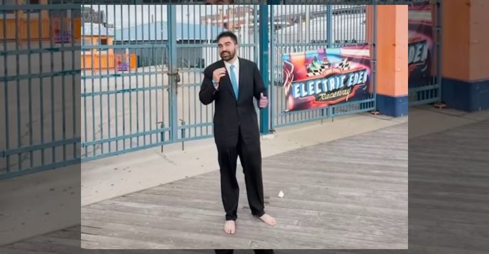 Zohran Mamdani em ato de campanha, vestindo terno e sem sapatos | Foto: Reprodução/Twitter/X