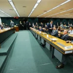 Audiência legislativa com parlamentares sentados em plenário durante discussão orçamentária em comissão
