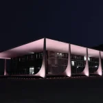 Fachada do Supremo Tribunal Federal iluminada à noite em Brasília, destacando arquitetura moderna e colunas curvas.