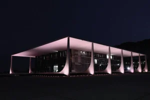 Fachada do Supremo Tribunal Federal iluminada à noite em Brasília, destacando arquitetura moderna e colunas curvas.