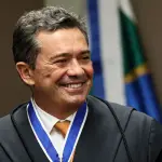 Magistrado brasileiro sorrindo durante cerimônia oficial, usando toga preta e medalha institucional no pescoço