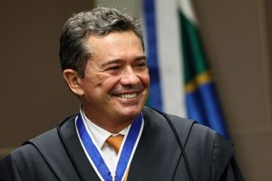 Magistrado brasileiro sorrindo durante cerimônia oficial, usando toga preta e medalha institucional no pescoço