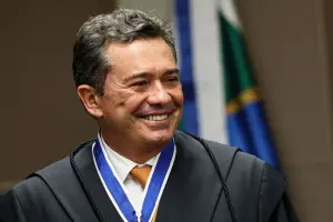 Magistrado brasileiro sorrindo durante cerimônia oficial, usando toga preta e medalha institucional no pescoço