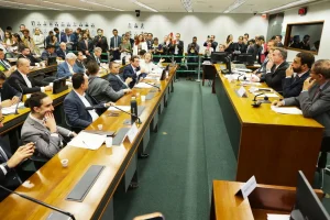 Reunião de comissão na Câmara dos Deputados com parlamentares sentados à mesa, debate em andamento e presença da imprensa.