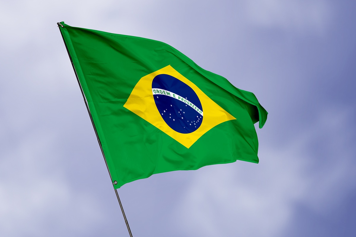 Bandeira do Brasil tremulando ao vento, com losango amarelo, círculo azul e a inscrição “Ordem e Progresso” sob céu nublado