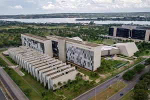 Vista aérea da sede do Superior Tribunal de Justiça em Brasília, com prédios modernos, áreas verdes e lago ao fundo.