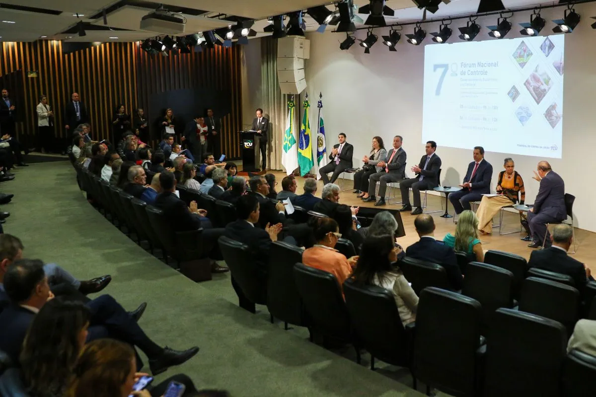 Evento institucional em auditório com autoridades sentadas no palco e público acompanhando fórum nacional