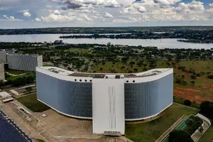 Vista aérea da sede do Tribunal Superior Eleitoral em Brasília, com edifício curvo, área verde ao redor e lago ao fundo.