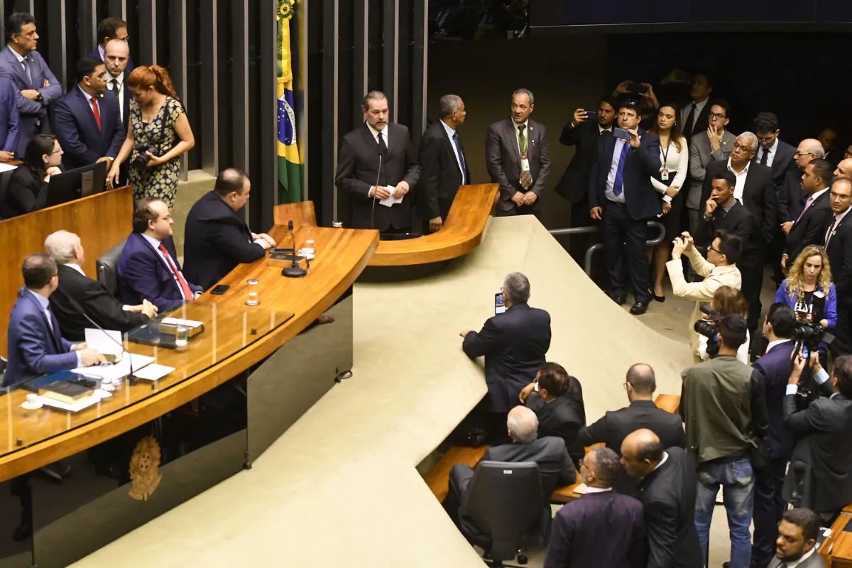 Parlamentar discursando no plenário da Câmara dos Deputados durante cerimônia oficial, com autoridades, imprensa e bandeira do Brasil ao fundo.