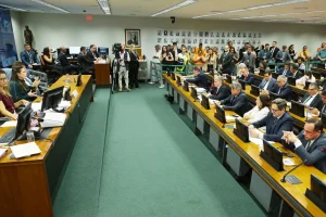 Audiência pública em comissão da Câmara dos Deputados com parlamentares sentados em plenário, imprensa e público acompanhando o debate.