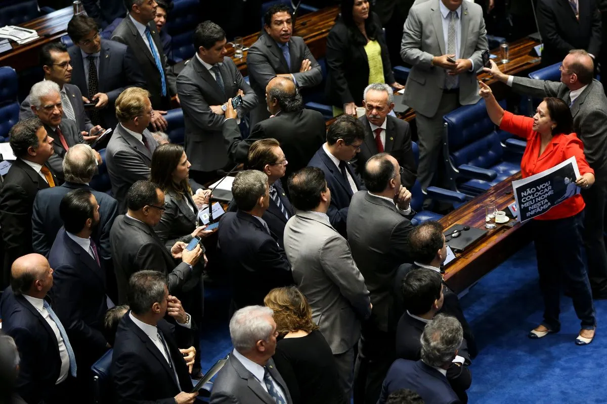 Parlamentares reunidos no plenário da Câmara dos Deputados durante momento de tensão, com deputada segurando cartaz e apontando em meio ao debate.