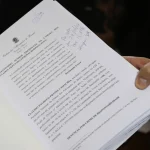 Documento oficial de pedido de impeachment sendo segurado por uma pessoa, com texto jurídico impresso e anotações manuscritas.
