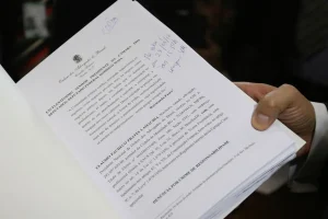 Documento oficial de pedido de impeachment sendo segurado por uma pessoa, com texto jurídico impresso e anotações manuscritas.